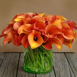 Orange calla lilies arranged in a green glass vase