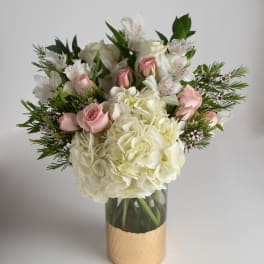 White hydrangeas and pink roses in a glass vase with greenery