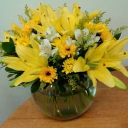 Yellow lilies and daisies in a round glass vase