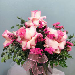 Pink-tipped white roses with bright pink filler flowers in a clear glass vase with a pink ribbon.