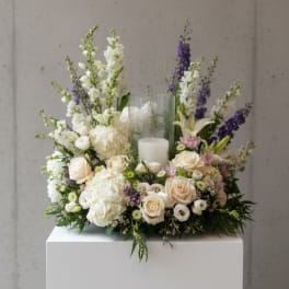 White and cream floral arrangement with purple accents around a candle