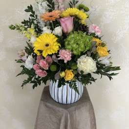 Mixed bouquet in a striped vase with yellow, pink, white, and peach blooms