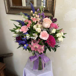 Mixed bouquet of pink, purple, and white flowers in a glass vase with a purple ribbon