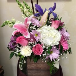 Mixed bouquet with pink and white lilies, roses, and purple flowers in a wooden basket