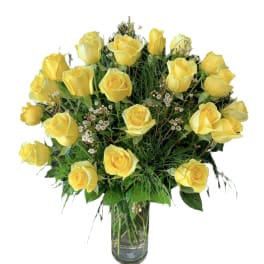 Tall arrangement of yellow roses with small white filler flowers in a clear glass vase