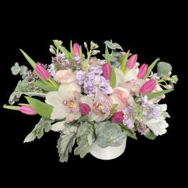 Low pastel arrangement with pink tulips, blush roses, orchids and lavender blooms in a white vase