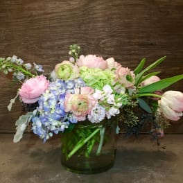 Pastel bouquet of hydrangeas, tulips, and ranunculus in a green glass vase