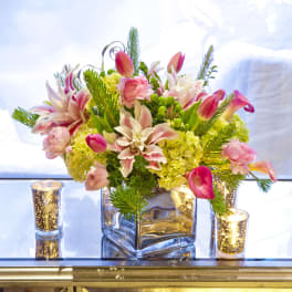 Pink tulips and lilies arranged in a square glass vase with candles