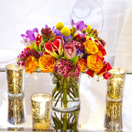 Colorful bouquet in a clear glass vase with gold candle holders
