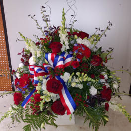 Large red, white, and blue floral arrangement with ribbon in a white container