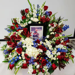 Large funeral wreath of red, white, and blue flowers with a framed photo in the center