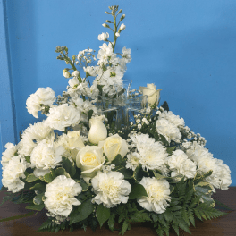 White roses, carnations, and mums arranged around a clear glass cross.