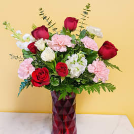 Red roses, pink carnations, and white blooms in a faceted red glass vase