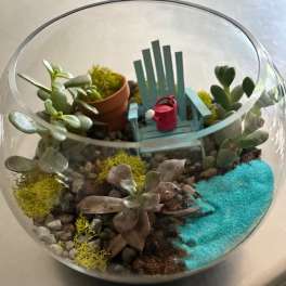Succulent terrarium in a glass bowl with a tiny chair and watering can