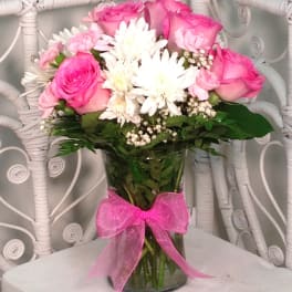 Pink roses and white daisies in a glass vase with a pink ribbon