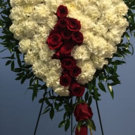 Heart-shaped standing spray of white carnations with cascading red roses on an easel.