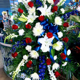 Large standing floral spray with red roses, white lilies, and blue ribbon
