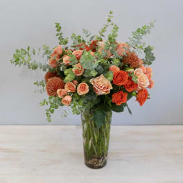 Tall glass vase of peach and orange roses with dahlias and eucalyptus accents