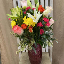 Mixed bouquet of roses, lilies, and chrysanthemums in a burgundy vase