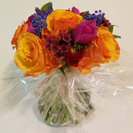 Bouquet of orange and yellow roses with purple accents in clear wrap