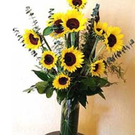 Tall arrangement of yellow sunflowers in a clear glass vase on a small round table