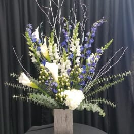 Tall floral arrangement with white calla lilies and blue-purple spikes in a wooden vase