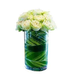 Cluster of white roses arranged in a tall glass cylinder vase lined with green leaves.