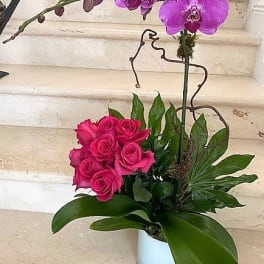 Tall orchid and hot pink rose arrangement in a white pot with lush foliage