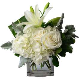 White lilies, roses, and hydrangeas arranged in a clear square vase
