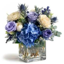 Blue and lavender floral arrangement in a clear square vase