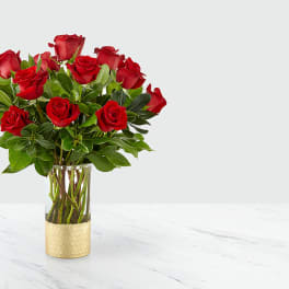 Red roses arranged in a clear glass vase with a gold base