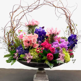 Large floral arrangement with pink, purple, and green blooms in a pedestal bowl