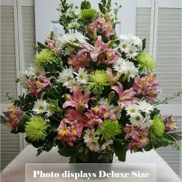 Tall arrangement of pink lilies, white daisies, and green mums in a dark vase