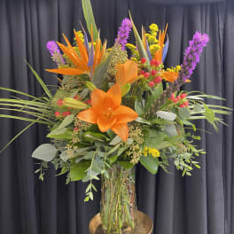 Tall tropical bouquet with orange lilies in a glass vase
