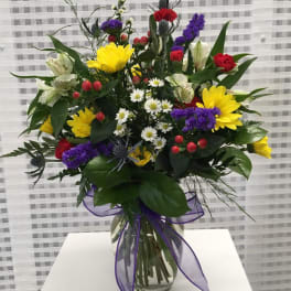 Mixed bouquet in a clear glass vase with yellow, purple, red, and white flowers