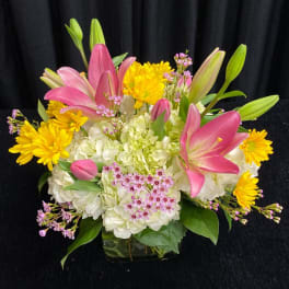 Pink lilies and yellow daisies arranged with white hydrangeas in a glass vase