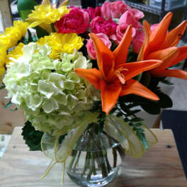 Bouquet of orange lilies, pink roses, yellow daisies, and pale hydrangea in a glass vase