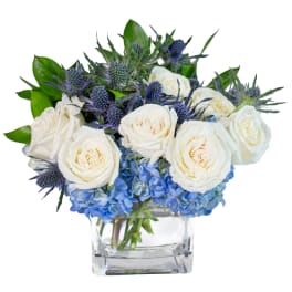 White roses and blue hydrangeas in a clear square vase