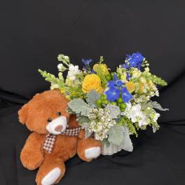 Bouquet of yellow, blue, and white flowers beside a teddy bear
