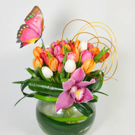 Tulip arrangement in a glass bowl with a pink orchid and butterfly decoration