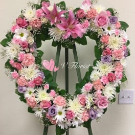 Heart-shaped standing wreath with pink lilies, roses, carnations, and white daisies on a green easel.