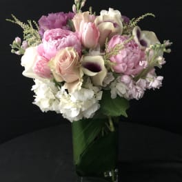 Tall arrangement of pink and white flowers in a clear glass vase lined with green leaves.