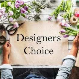 Hands hold a Designers Choice sign on a table surrounded by loose pink and purple tulip stems and tools.