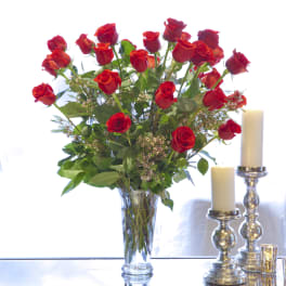 Red roses arranged in a clear glass vase beside white candles
