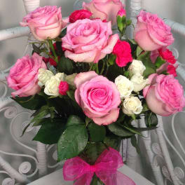 Pink and white roses arranged in a glass vase with a pink bow.
