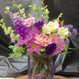 Mixed bouquet of pink, purple, and white flowers in a purple glass vase