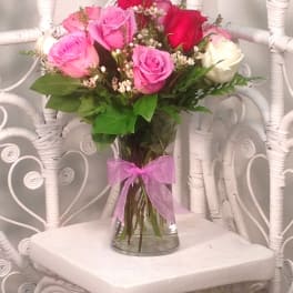 Bouquet of pink, red, and white roses in a glass vase with a pink ribbon