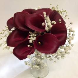 Deep burgundy calla lilies in a clear glass vase with white baby's breath