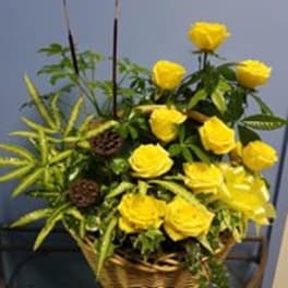 Yellow roses arranged in a woven basket with spiky green foliage