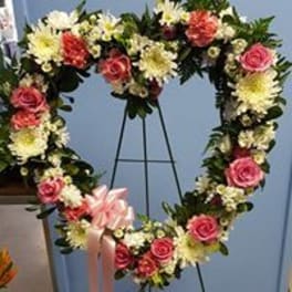 Heart-shaped floral wreath with pink roses and white flowers on a stand